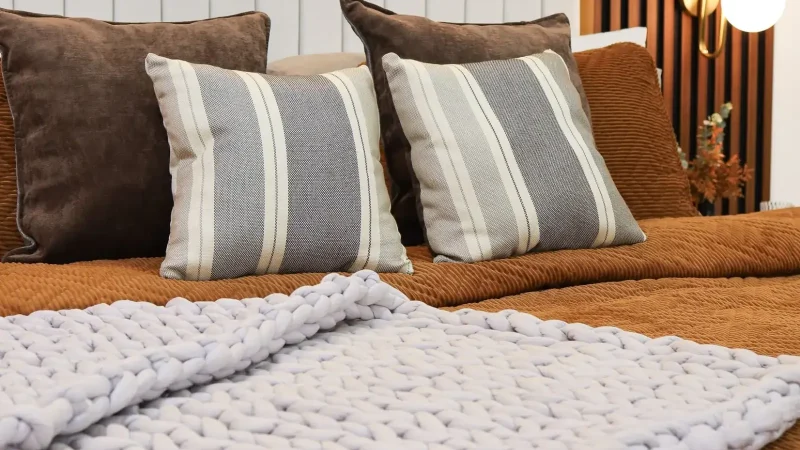 Cosy bed with a chunky knitted throw and warm lamp light in a rented bedroom